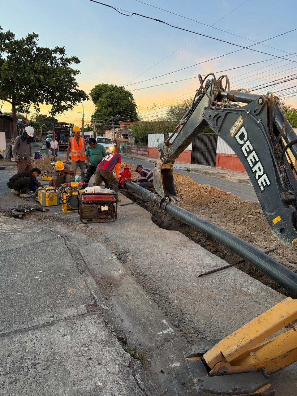 Cuadrilla de AMALEMO instalando una línea de agua potable con excavadora al atardecer